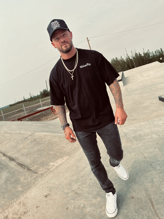 Model walking in black organic high neck tee by Wolves Cry, styled with dark denim and white sneakers for bold streetwear appeal.