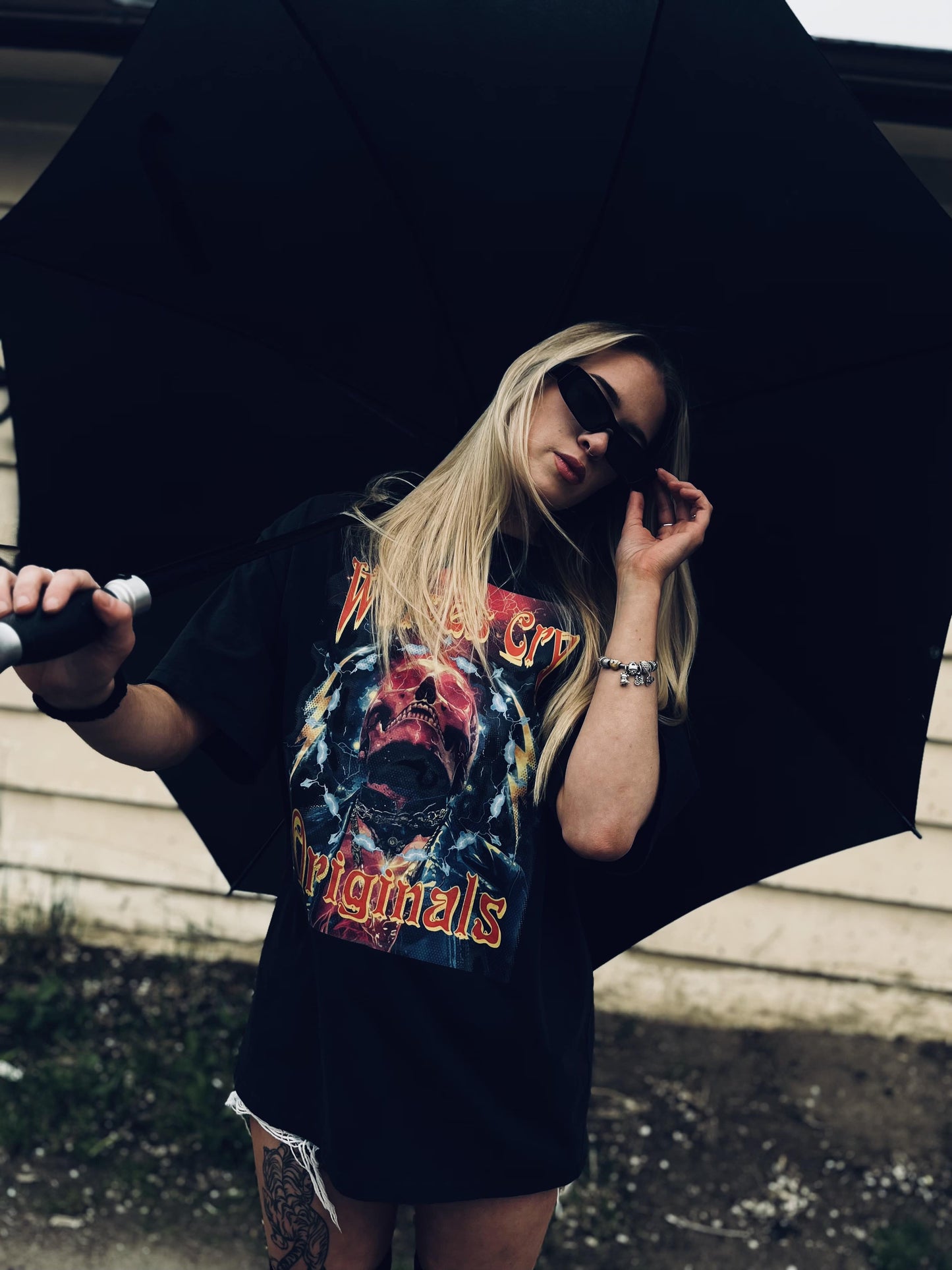 Woman wearing Wolves Cry Oversized Universe Tee under an umbrella, with tattoo and shorts visible, styled for unisex grunge aesthetic.