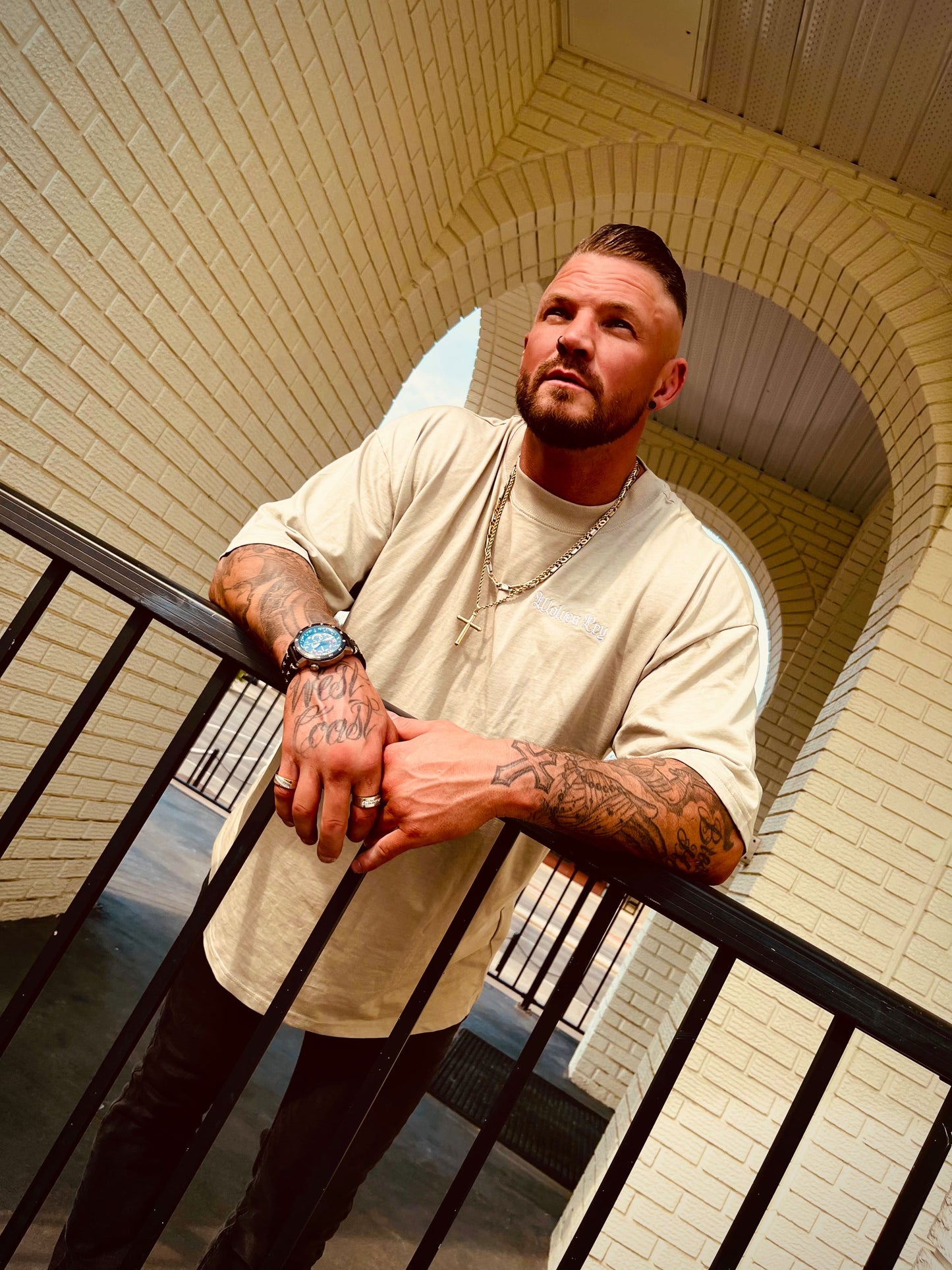 Model standing in front of arched brick wall in sage dust Wolves Cry tee, highlighting the oversized streetwear silhouette.