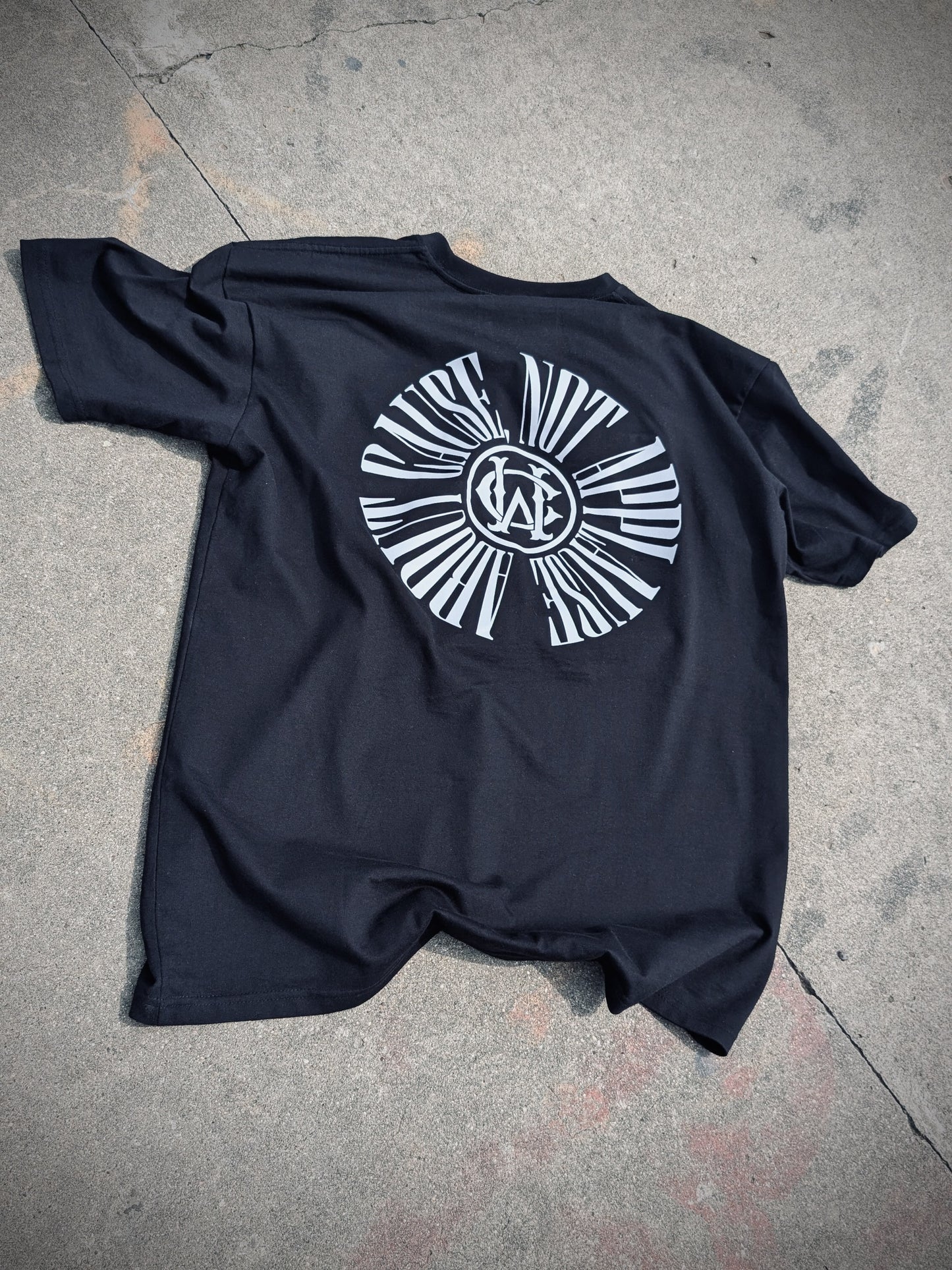 Black tee shirt laid flat showcasing bold back design: “About Cause Not Applause” graphic.