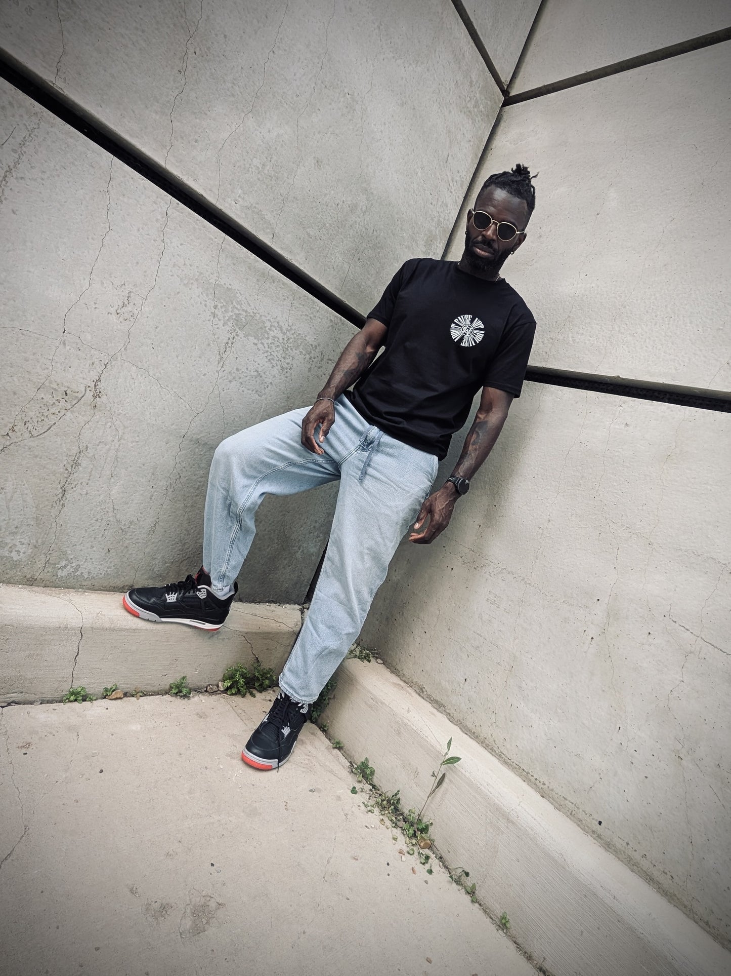 Full-body shot of model leaning against wall in black WC tee and light jeans.