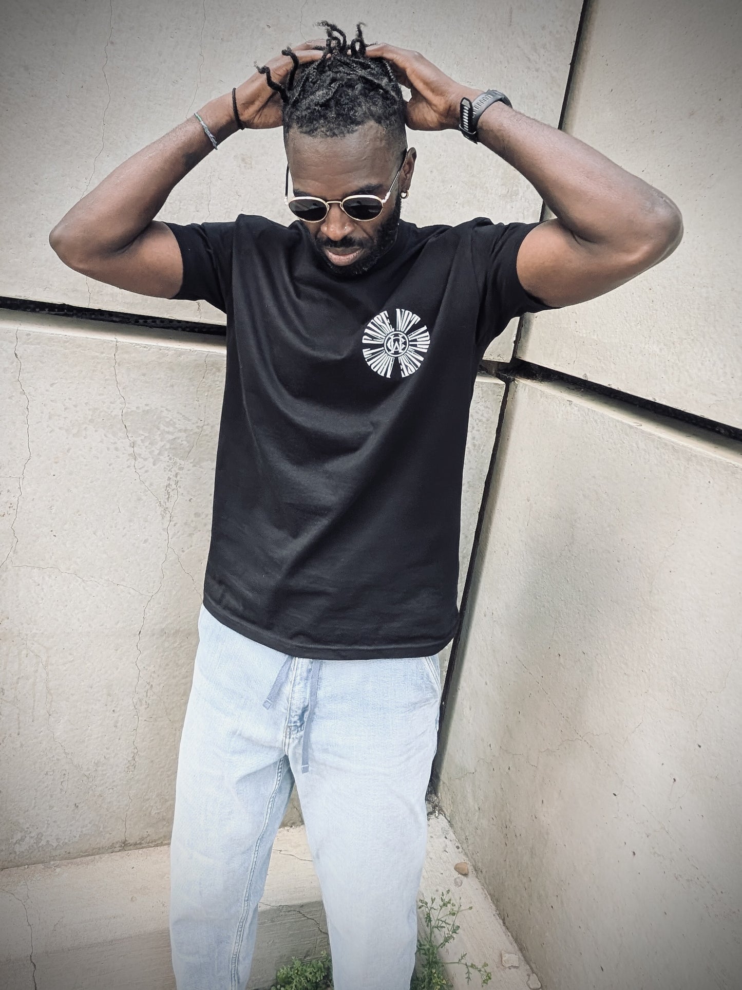 Model wearing black WC About Cause Tee with light denim and sunglasses, hands in hair.