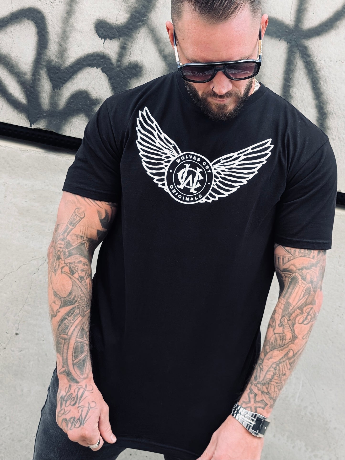 Streetwear t-shirt for men — Wolves Cry Flight Academy Tee in black with winged monogram logo, relaxed fit and bold graphic, urban fashion look.