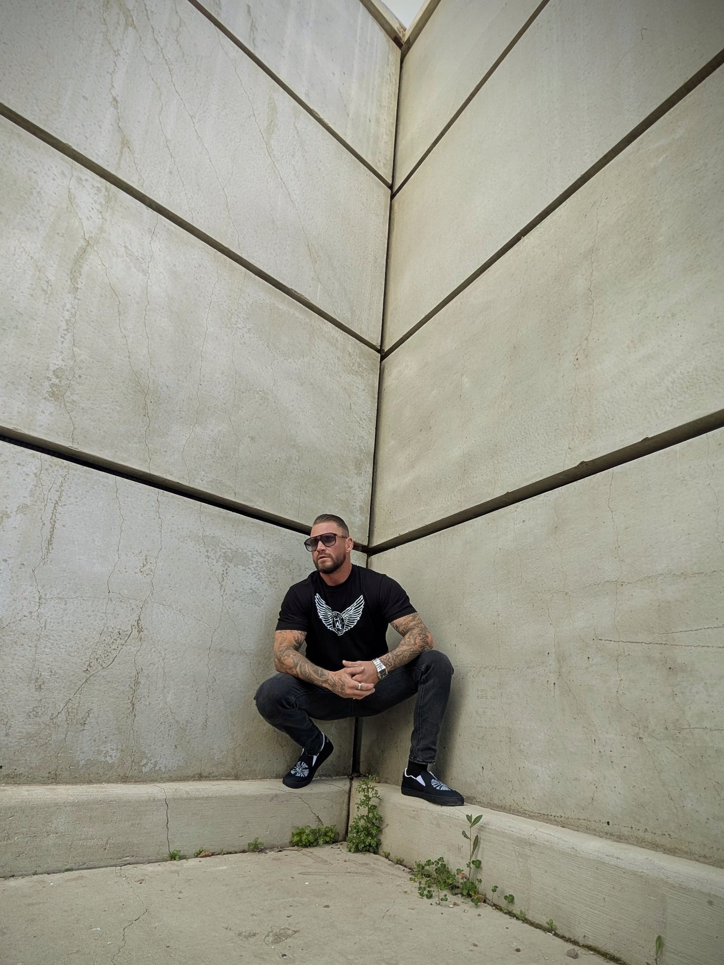 Model squatting in corner wearing black Wolves Cry tee, sharp streetwear styling