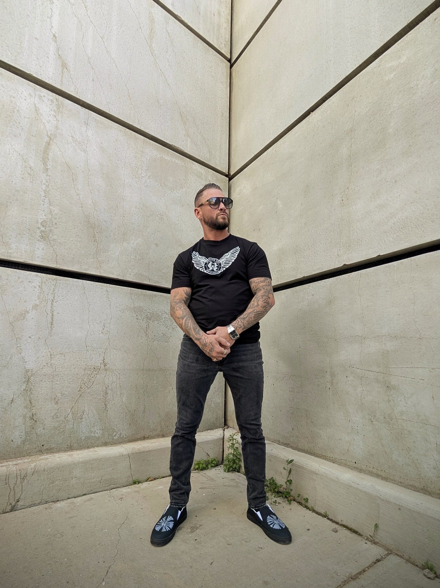 Model standing in corner wearing black tee with winged Wolves Cry logo, clean silhouette