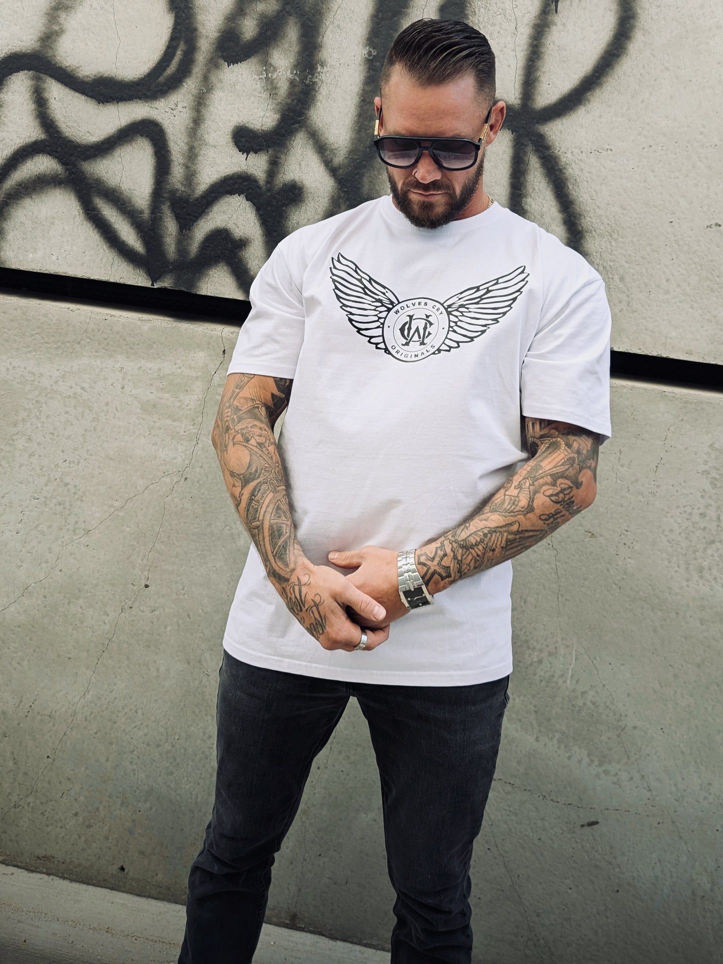 Side view of model in white WC Flight Academy Tee, styled against concrete wall with graffiti backdrop.