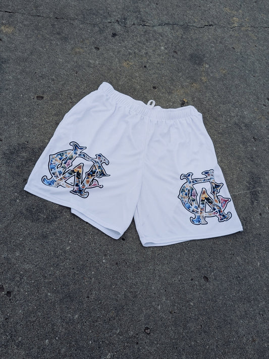 White WC Shadow Floral Mesh Shorts with full-color gothic logos in outdoor flat lay on concrete
