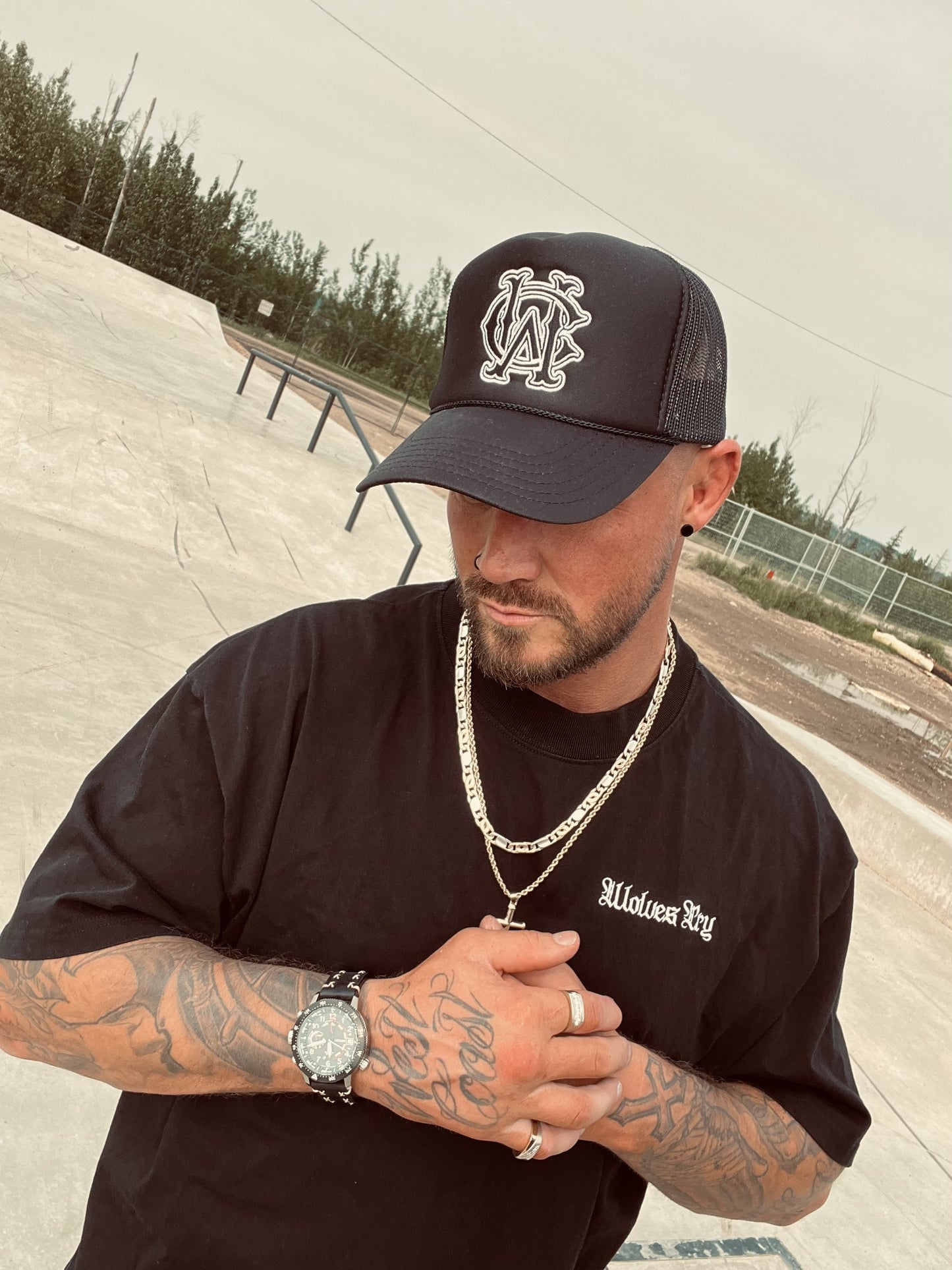 Model wearing the Wolves Cry Shadow Stitch Monogram Hat in black at skatepark – close-up angle showing detailed embroidery and streetwear chain styling.