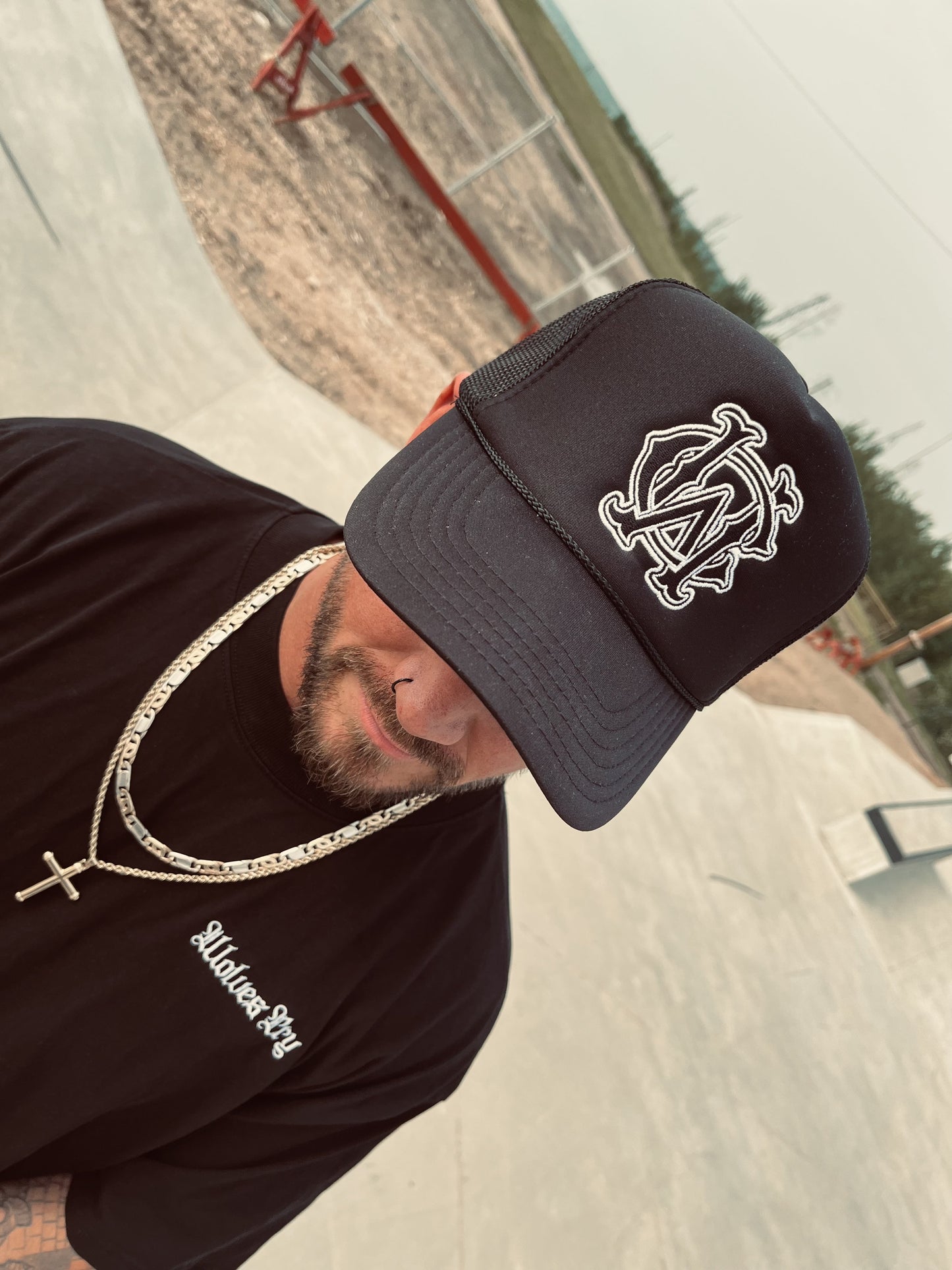 Wolves Cry Shadow Stitch Monogram Hat in black styled with matching tee and jewelry – wide skatepark setting, streetwear look.