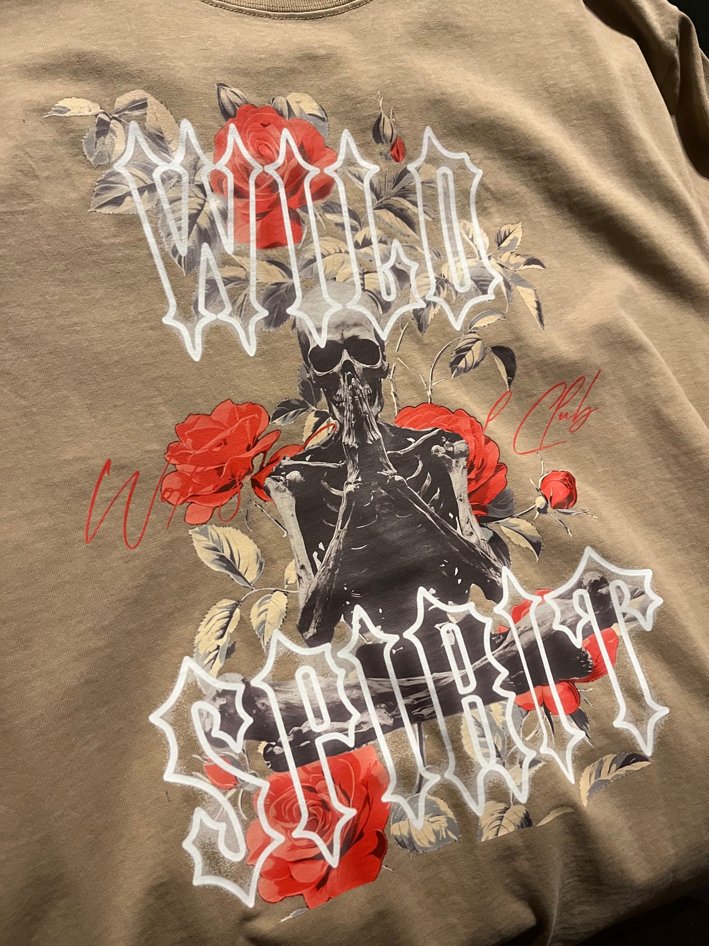 Close-up of the Wild Spirit Prayer Tee in khaki highlighting the red roses and meditating skeleton artwork with gothic Wild Spirit text.