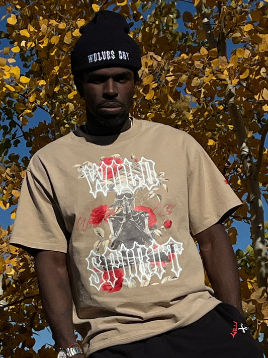 Male model, 6’1”, 195 lbs, wearing the Wild Spirit Prayer Tee in khaki with bold rose and skeleton print, paired with Wolves Cry beanie.