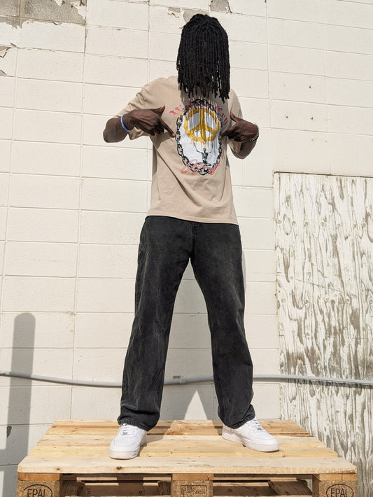 Model wearing Wolves Cry Endless Peace Tee in khaki, standing outdoors against a concrete wall — relaxed fit, heritage artwork, and quiet rebellion in motion.