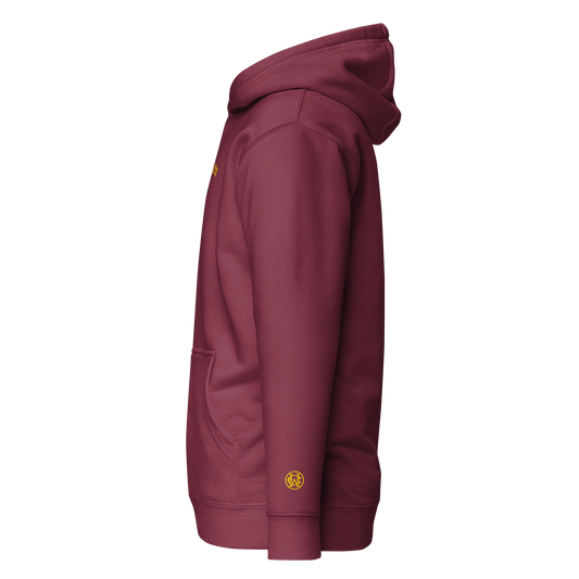 Side angle showing gold wrist monogram on maroon hoodie — subtle, powerful, and refined.