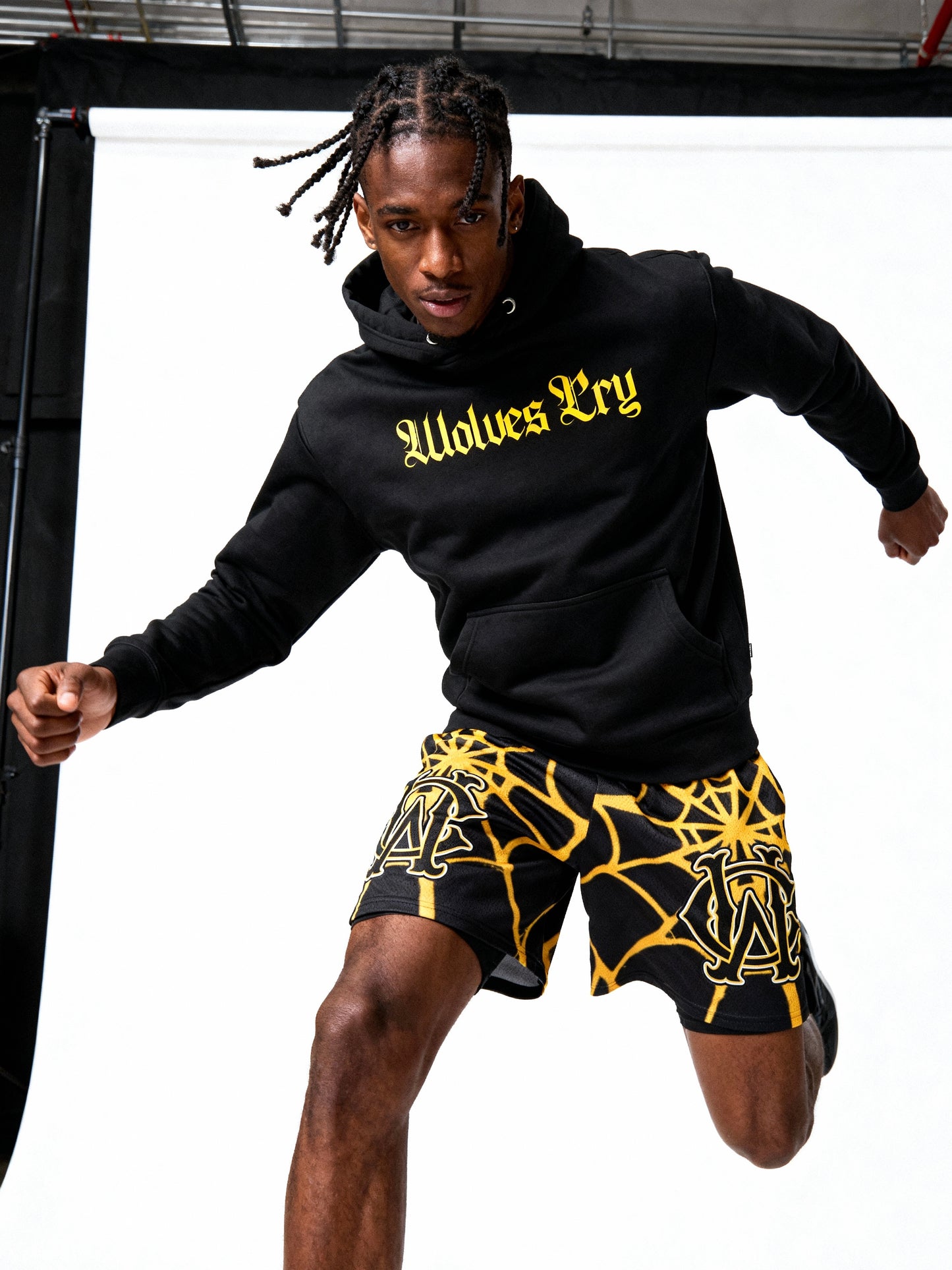 Person wearing a black hoodie with 'Wolves Cry' text and black shorts with yellow patterns.
