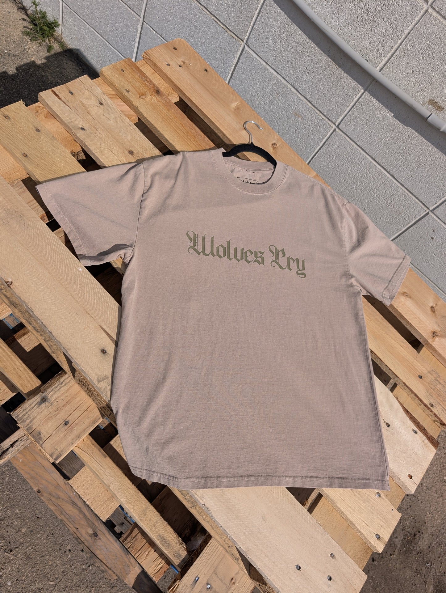 Flat lay of Wolves Cry Oversized Khaki Tee with subtle olive spell-out graphic — earthy neutral tones with a worn-in vintage wash.
