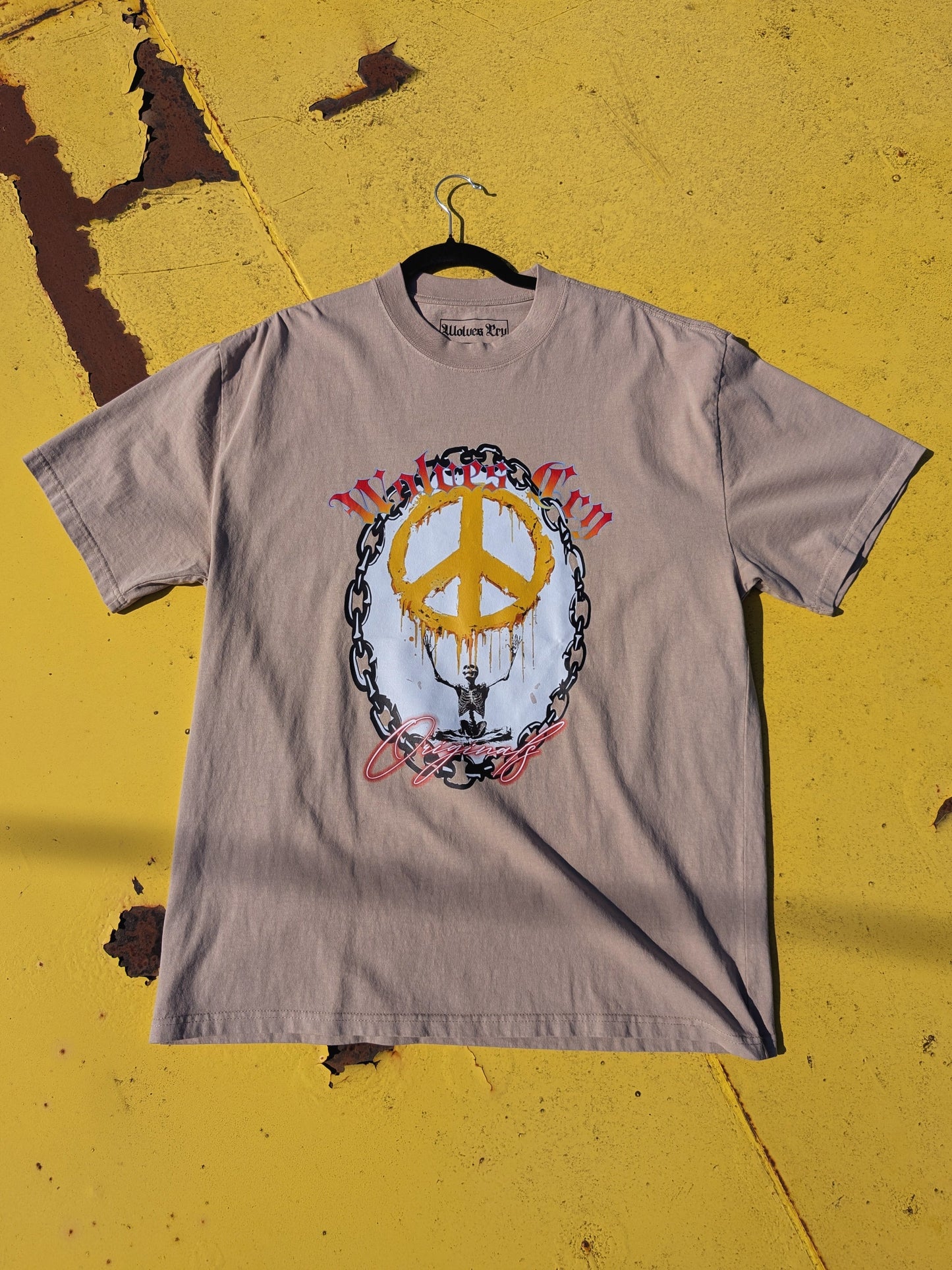 Flat lay of Wolves Cry Endless Peace Tee in khaki, highlighting peace-skull graphic surrounded by roses — tonal harmony and worn-in authenticity.