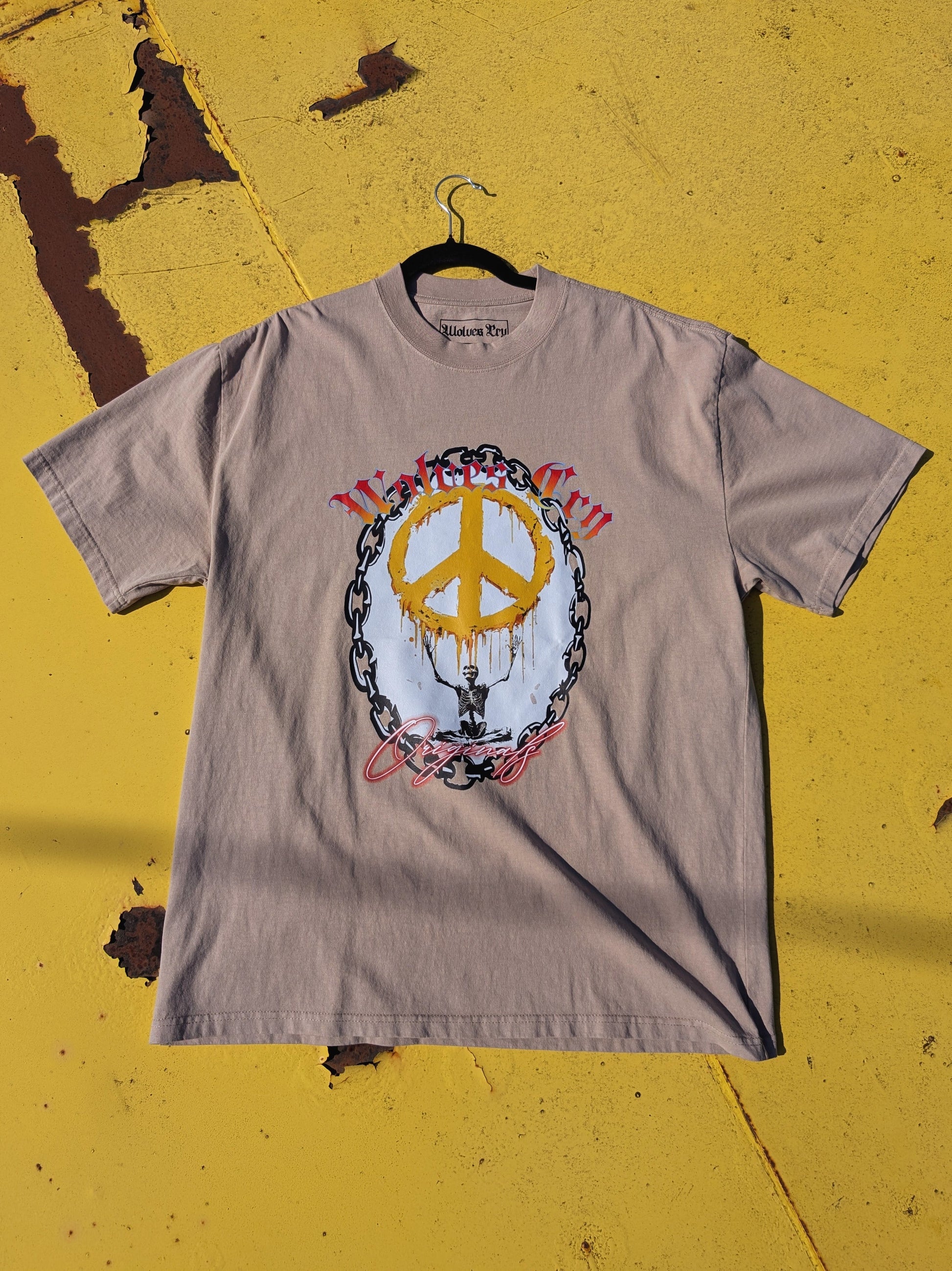 Flat lay of Wolves Cry Endless Peace Tee in khaki, highlighting peace-skull graphic surrounded by roses — tonal harmony and worn-in authenticity.