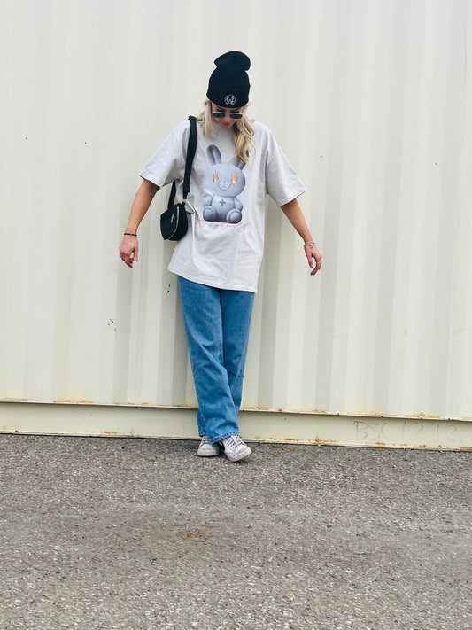 Full-body shot of the Wolves Cry Oversized Teddy Tee in bone off-white, paired with blue jeans and a black beanie, showcasing the relaxed oversized fit.
