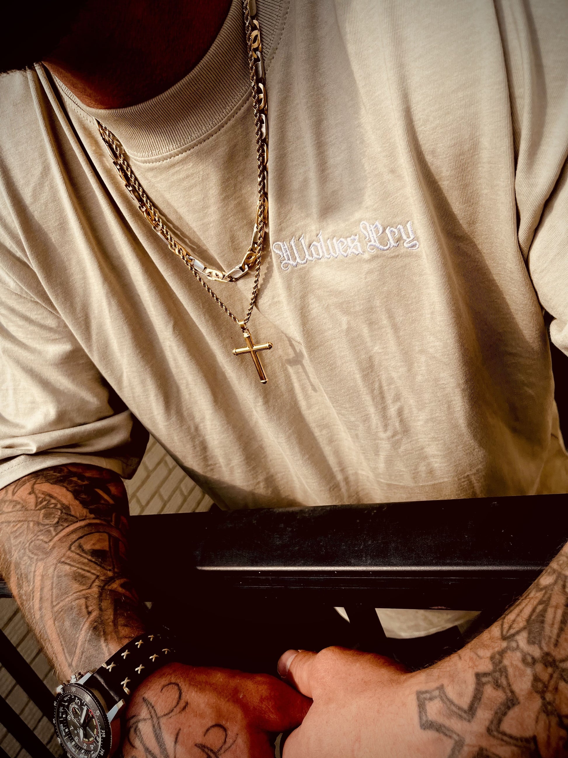 Close-up of the embroidered Wolves Cry logo on the sage dust organic high neck drop tee, styled with layered gold chains.