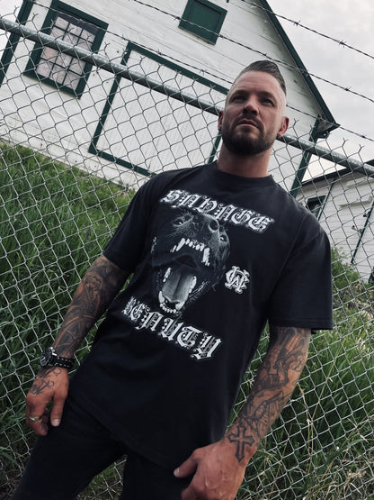 Male model wears Wolves Cry Savage Beauty Tee styled with all-black streetwear in front of chainlink fence