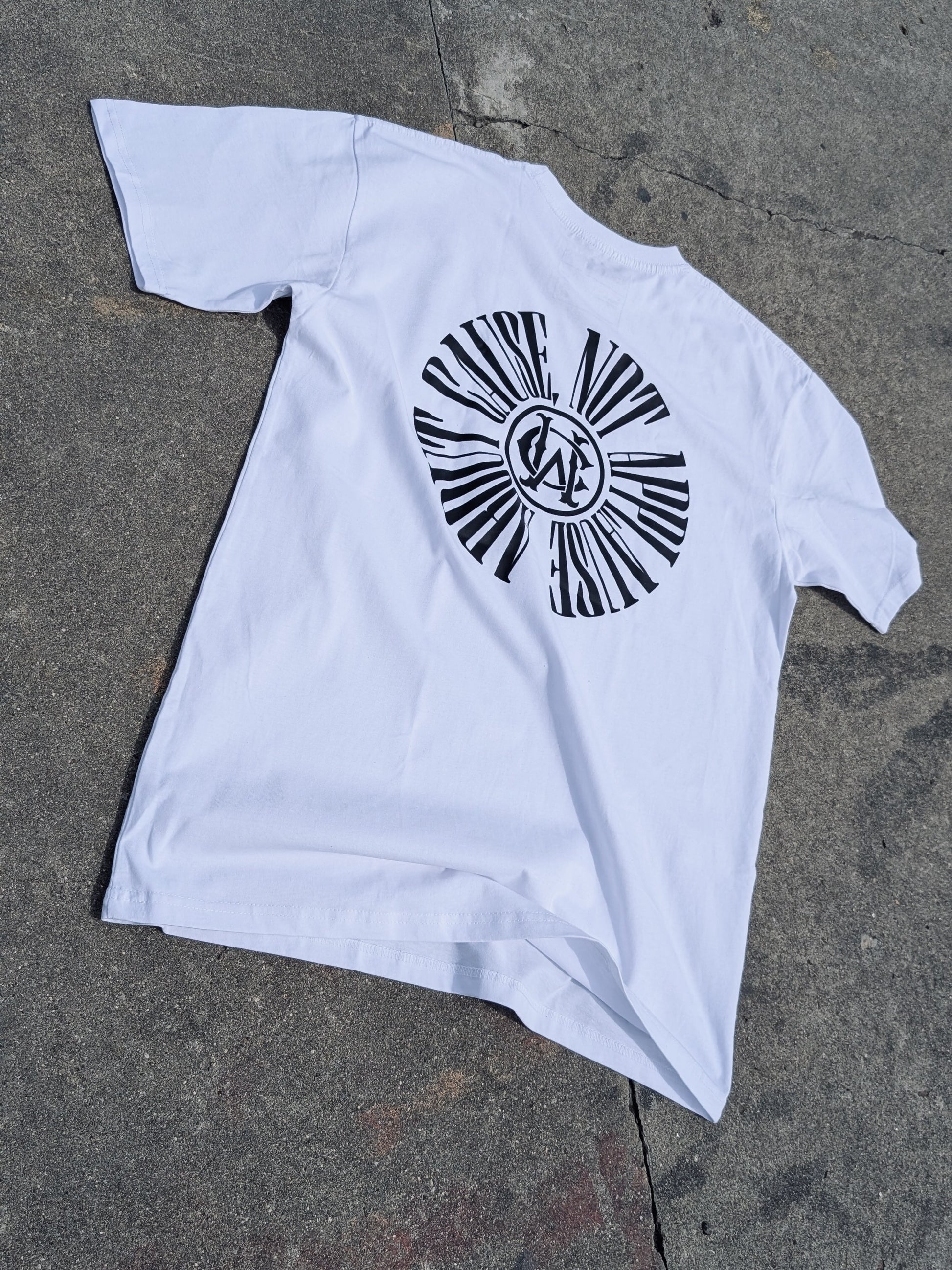 White graphic tee with full circular “About Cause Not Applause” print on back, street-style lay flat