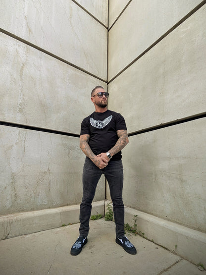 Model standing in corner wearing black tee with winged Wolves Cry logo, clean silhouette