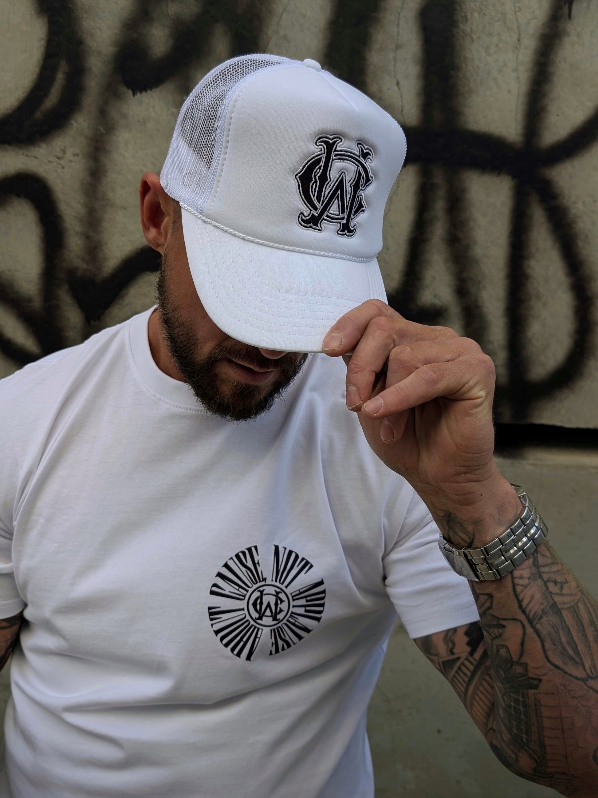 White WC foam trucker hat styled with graphic tee — streetwear look featuring black embroidered monogram