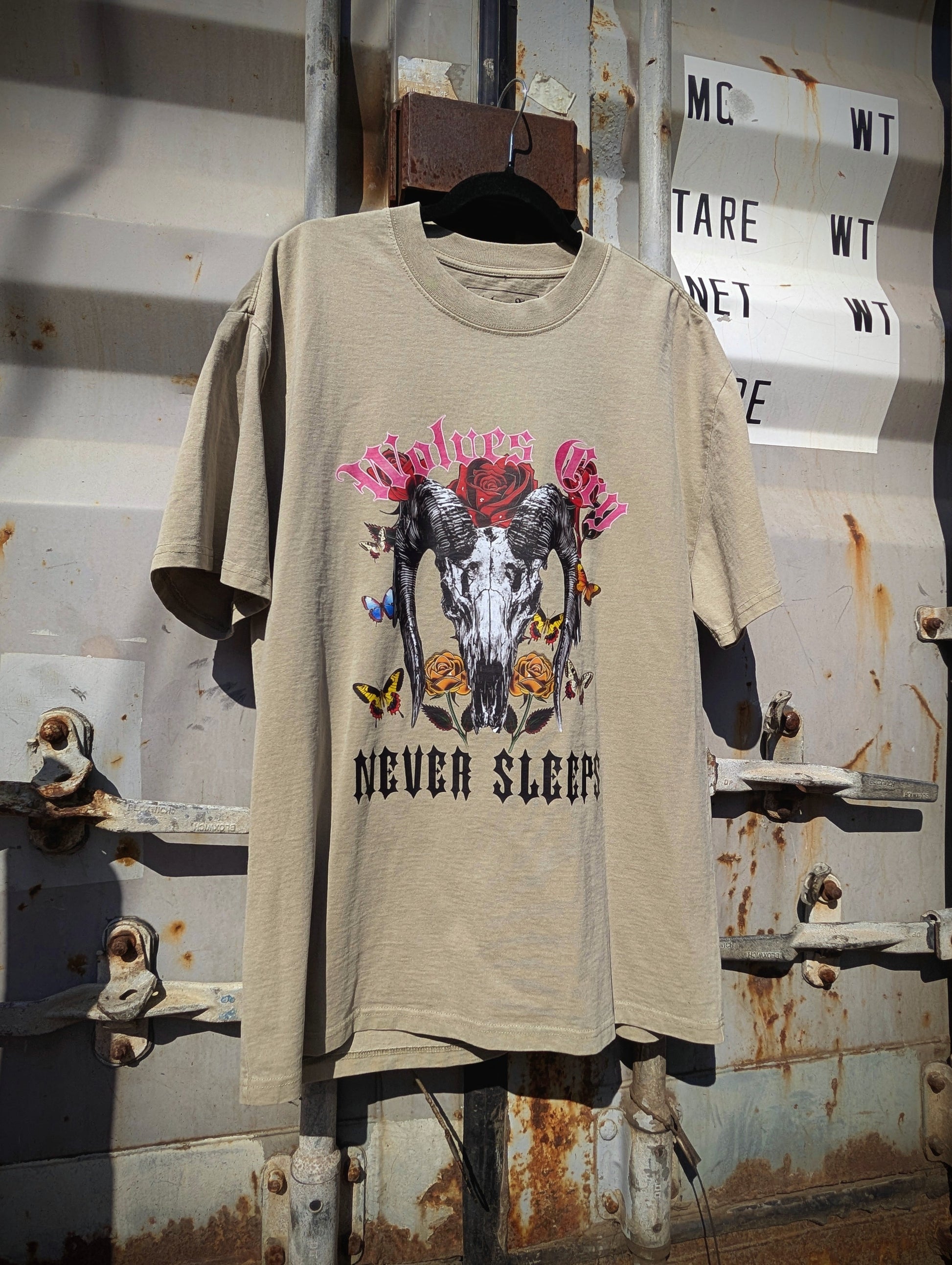 Flat lay of Wolves Cry DVNS Tee in sage green — showcasing the detailed “Never Sleeps” motif and soft washed cotton finish for a lived-in aesthetic.