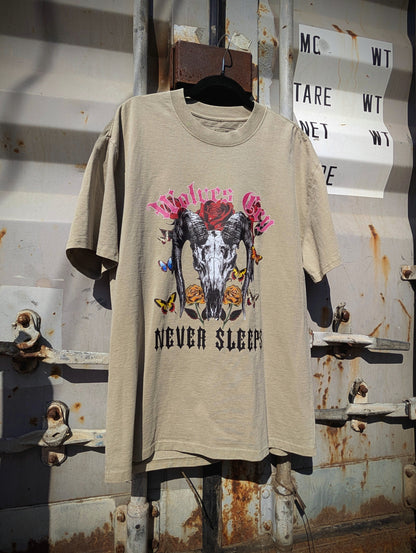 Flat lay of Wolves Cry DVNS Tee in sage green — showcasing the detailed “Never Sleeps” motif and soft washed cotton finish for a lived-in aesthetic.