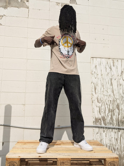 Model wearing Wolves Cry Endless Peace Tee in khaki, standing outdoors against a concrete wall — relaxed fit, heritage artwork, and quiet rebellion in motion.