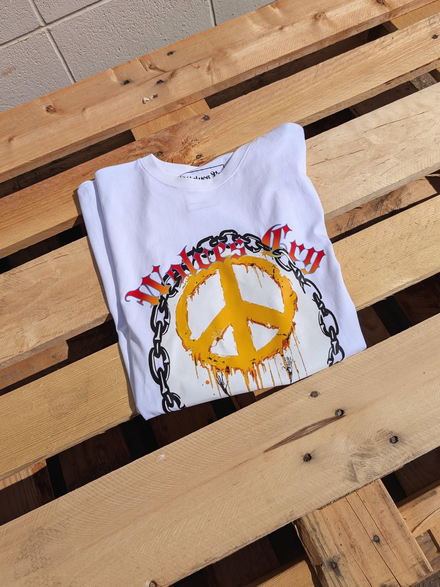 Flat lay of Wolves Cry Endless Peace Tee in white on wooden boards, highlighting the peace-skull and rose artwork with vibrant yellow and red tones for an authentic streetwear finish.