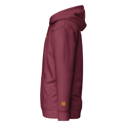 Side angle showing gold wrist monogram on maroon hoodie — subtle, powerful, and refined.
