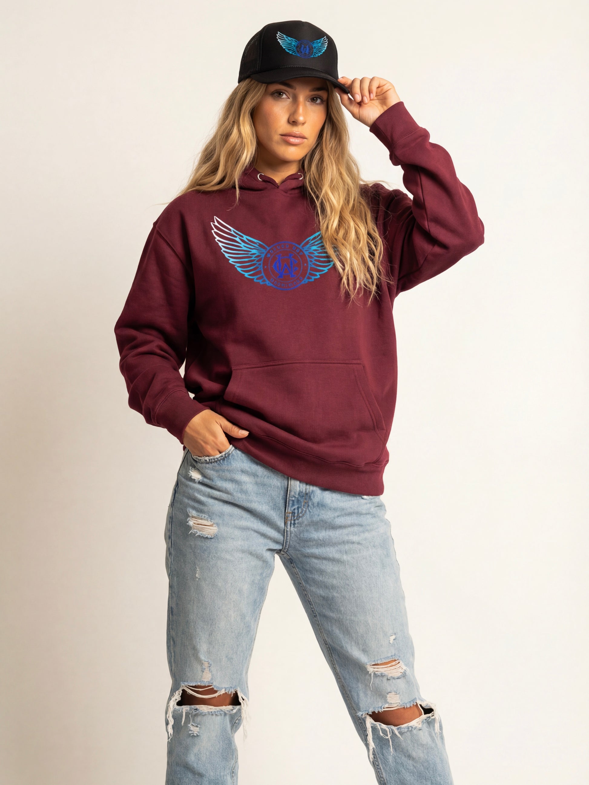 Person wearing a maroon hoodie with a blue logo and light blue jeans on a beige background