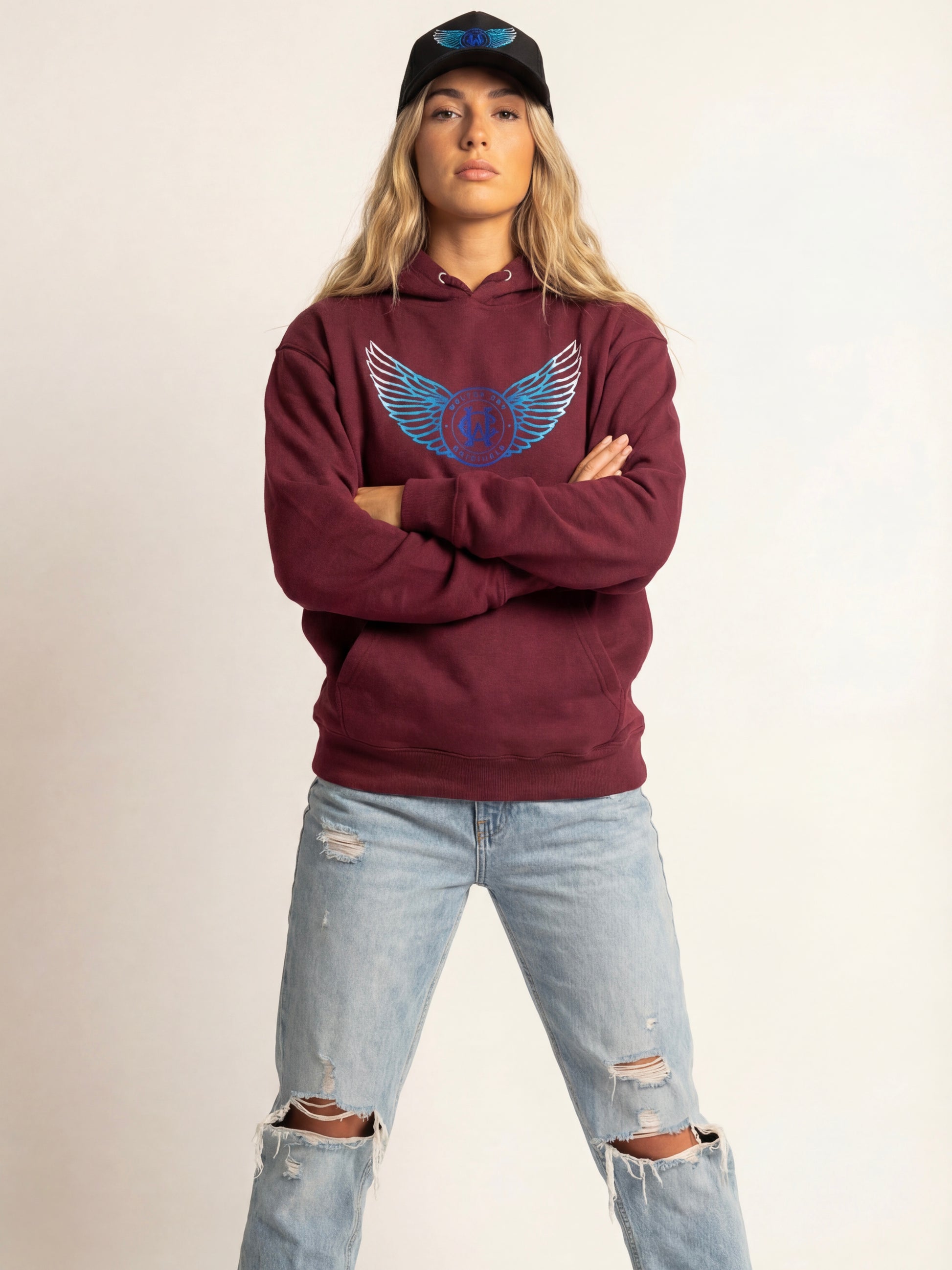 Person wearing a maroon hoodie with a blue logo and light blue jeans on a plain background