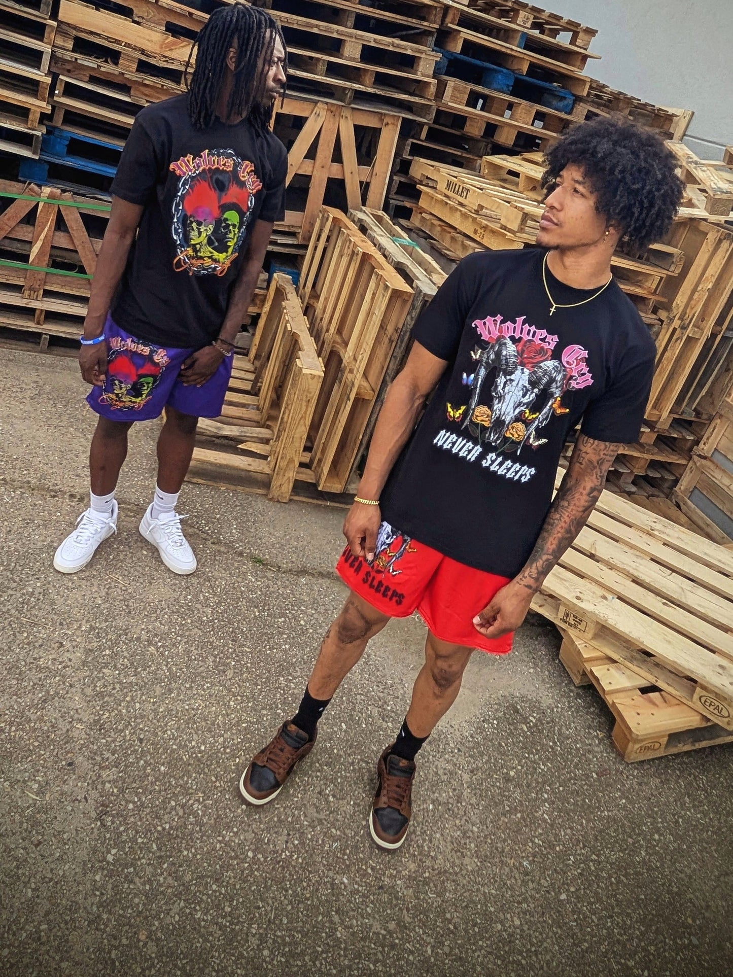 Outdoor lifestyle shot of Wolves Cry Megadeath Tee in black, layered with red shorts and urban background textures, merging classic metal-inspired artwork with modern streetwear tone.