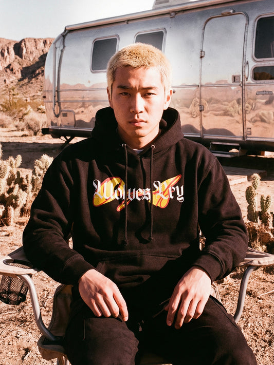 Person wearing a black hoodie with 'Wolves cry' logo in a desert setting with a trailer.