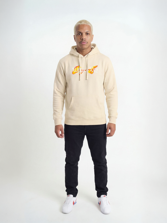 Person wearing a beige hoodie with a logo and dark pants on a white background