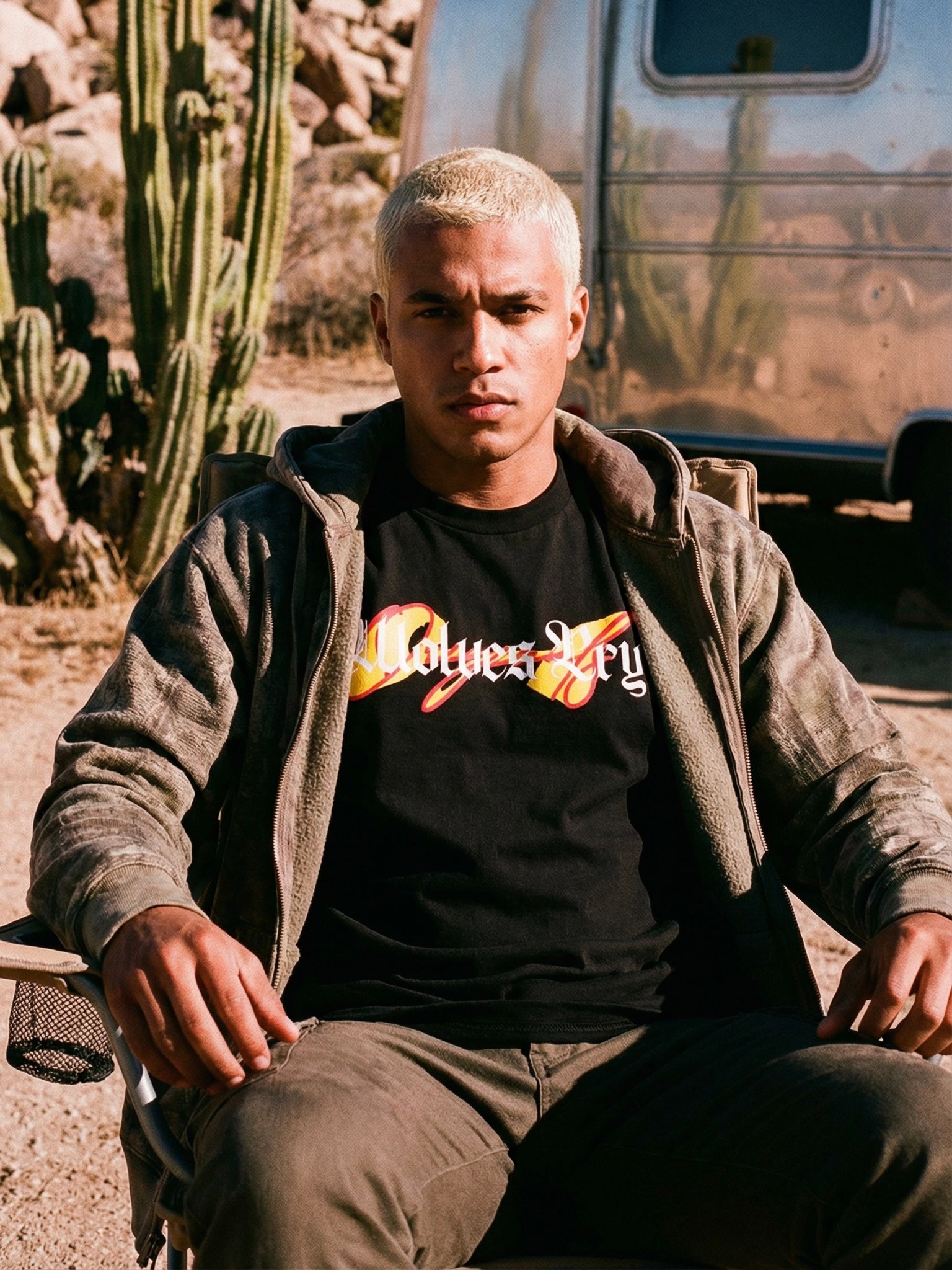 Person sitting outdoors with cacti and a trailer in the background